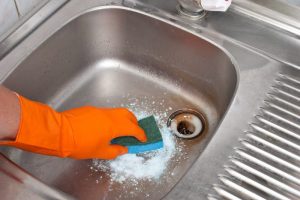 Wearing orange glove cleaning the sink.