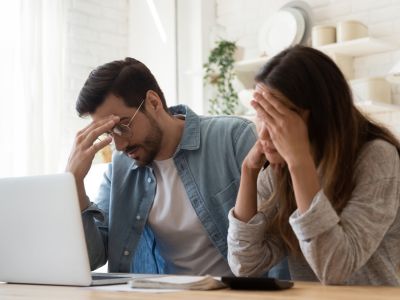 Frustrated couple reviewing high utility bills on laptop, indicating potential water heater issues, related to plumbing maintenance in Oak Park and Wixom, MI.