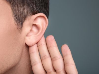 Person listening attentively with hand cupped behind ear, relating to strange sounds from a water heater system.
